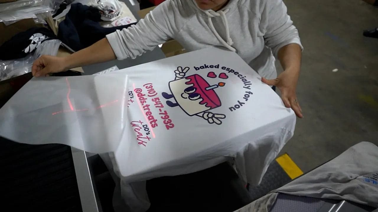 Person holding white t-shirt with printed design demonstrating hot peel transfer technique for print shops