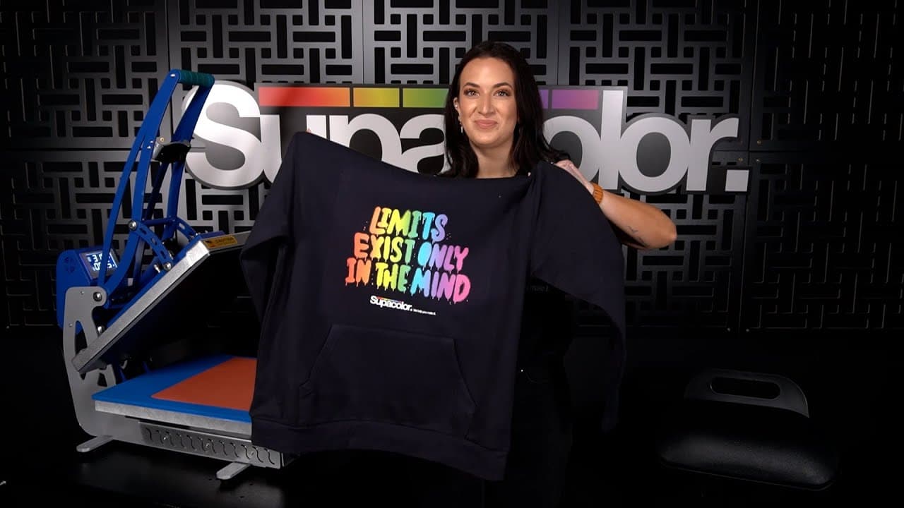 Woman displaying printed fleece hoodie with colorful text on Supacolor heat press machine