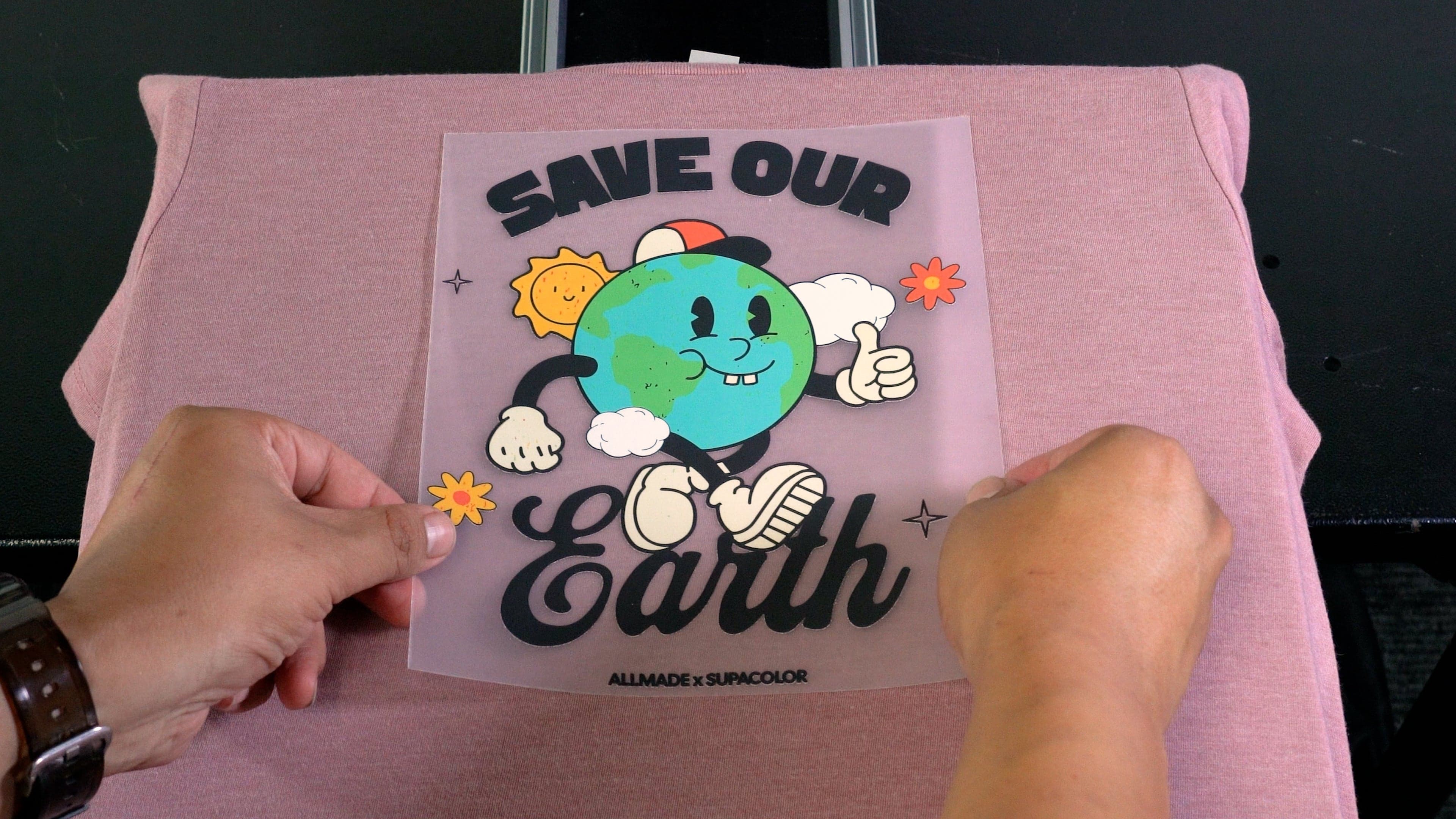 Hands holding pink eco-friendly t-shirt with "Save Our Earth" graphic design by Allmade x Supacolor